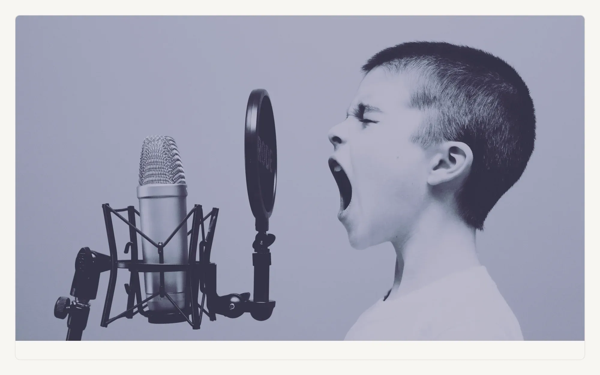 Duotone photograph of a child singing into a studio microphone.